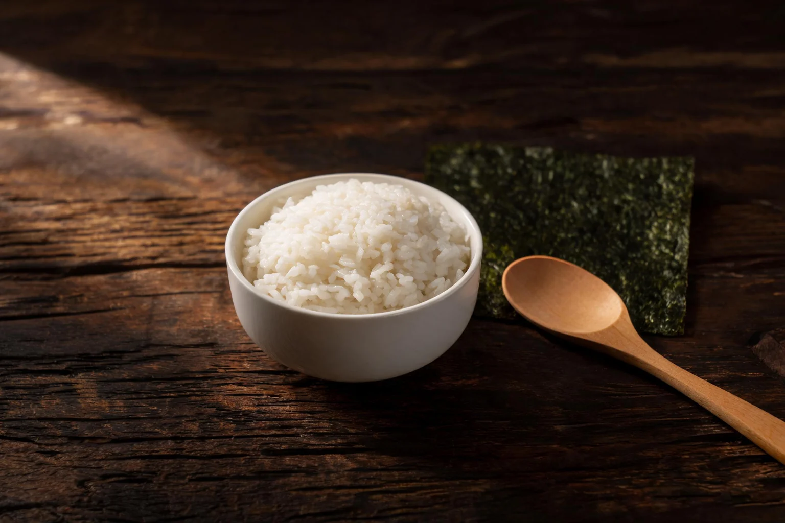Un bol de riz blanc, une feuille de nori et une cuillère en bois. (image d'illustration)